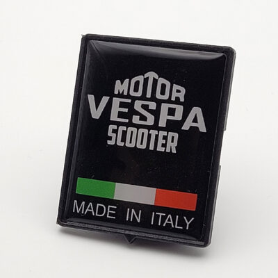 Schwarzes rechteckiges Emblem mit der weißen Aufschrift „Motor Vespa Scooter“, darunter eine kleine italienische Flagge und der Text „Made in Italy“.