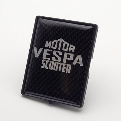 Schwarzes 3D-Vespa-Piaggio-Emblem in Carbon-Optik mit silbernem „Motor Vespa Scooter“-Schriftzug.