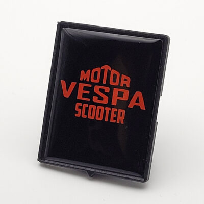 Schwarzes Vespa-Piaggio-Emblem mit orangefarbenem „Motor Vespa Scooter“-Schriftzug in glänzender 3D-Optik.