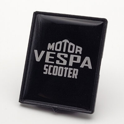 Schwarzes 3D-Vespa-Piaggio-Emblem mit weißem „Motor Vespa Scooter“-Schriftzug auf glänzender Oberfläche.