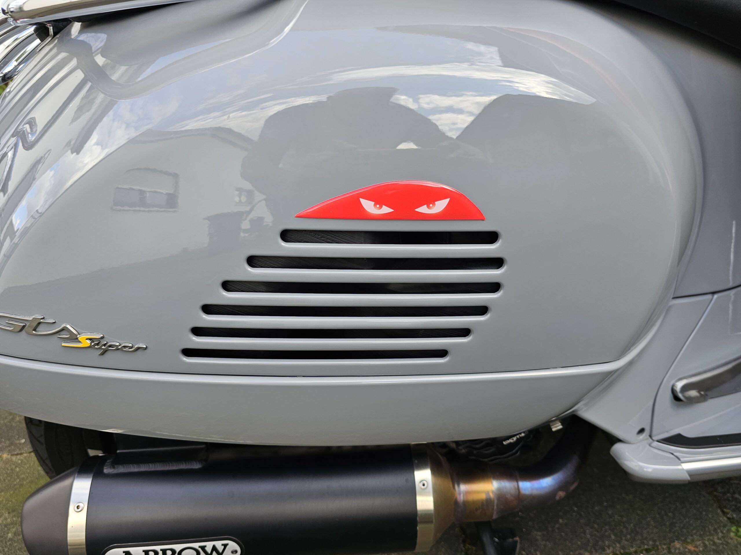 Rotes „Red Eyes“-Emblem an der Seitenbacke einer Vespa GTS montiert, als dekoratives 3D-Detail.