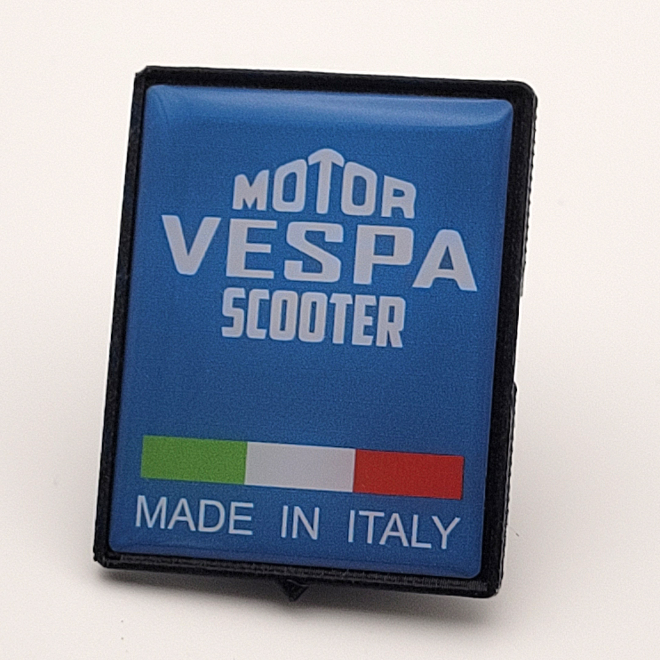Photographed blue 3D Vespa Motor Scooter Made in Italy emblem shown at an angle with black border.