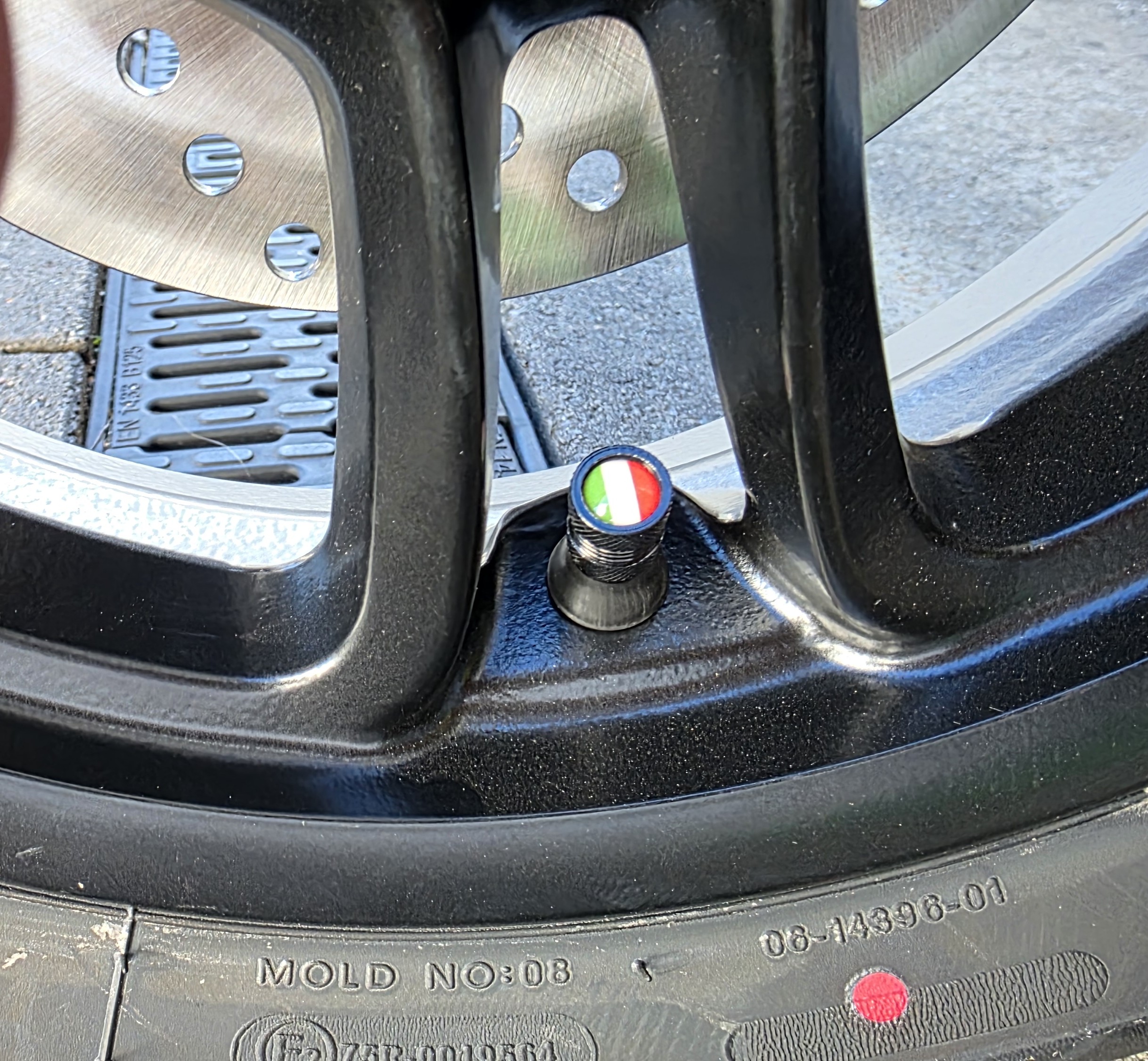 Schwarze Ventilkappe mit italienischer Flagge, montiert auf einem Reifenventil an einer schwarzen Felge.